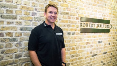 John Smit standing in front of a brick wall with the robert walters logo on it