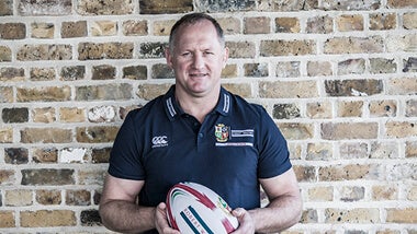 richard hill in a rugby shirt holding a rugby ball against a brick wall