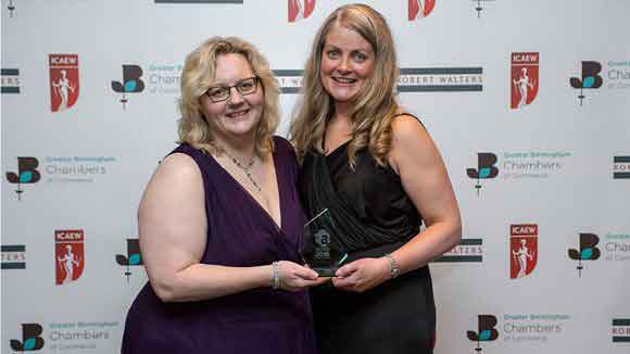 Two females in front of the award partners back drop holding an award