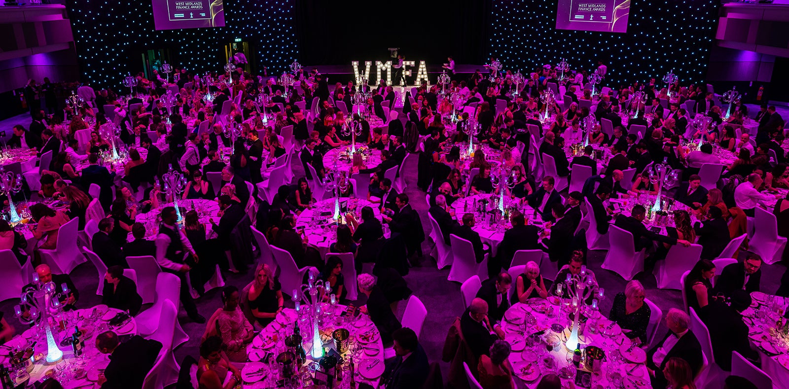 Large room with many people sitting at round tables and the letters WMFA at the front for the West Midlands Finance Awards’