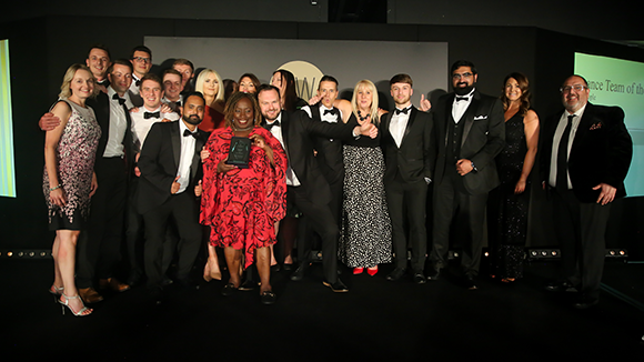 finance awards winners in black tie attire and dresses in front of the sponsors marquee posing for photo