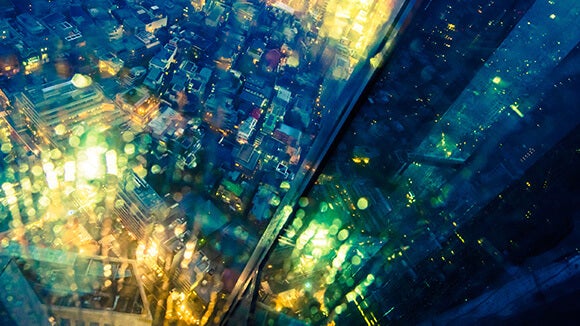 blue and green lights in city, looking down from top floor of glass building