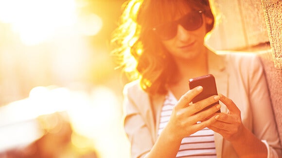 woman outside with sunglasses on in sunshine using mobile phone 