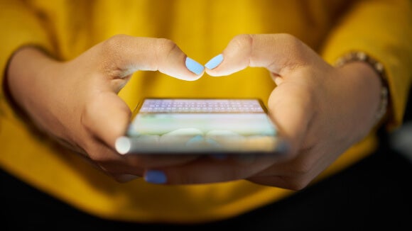 woman with blue nails and yellow top typing a message on social media