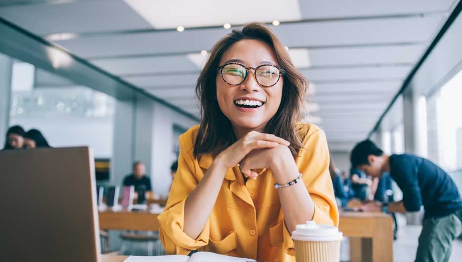 Portrait of excited hipster student in classic glasses for vision protection feeling excited and laughing during free time in university classroom, happy smiling Chinese woman e learning indoors
