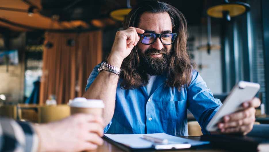 Positive bearded caucasian male using mobile phone for checking banking account owning small business, smiling mature man in spectacles for vision correction satisfied with getting good news via mail