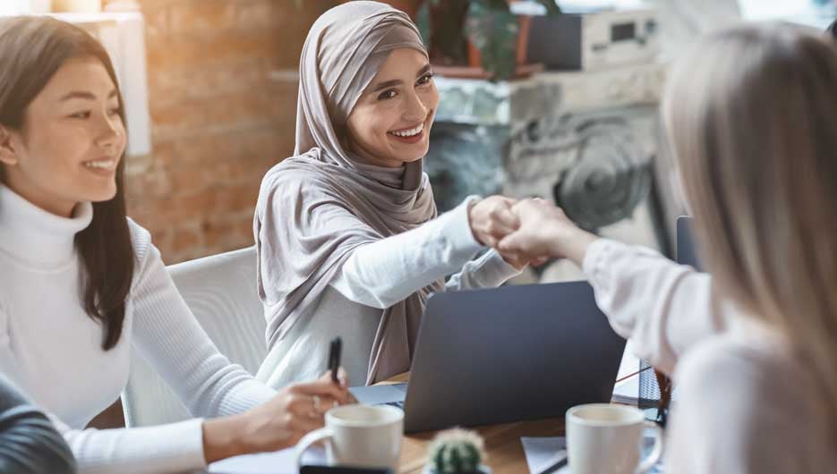 Two multiracial girls business colleagues shaking hands during group meeting in office, close up